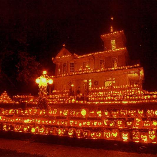 Multi-story house decorated with glowing carved pumpkins at night
